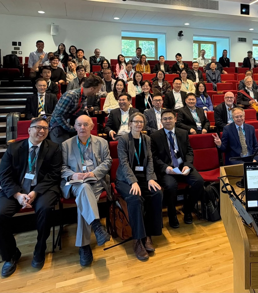 Conference participants seated in a tiered lecture hall at the University of Cambridge, smiling toward the camera